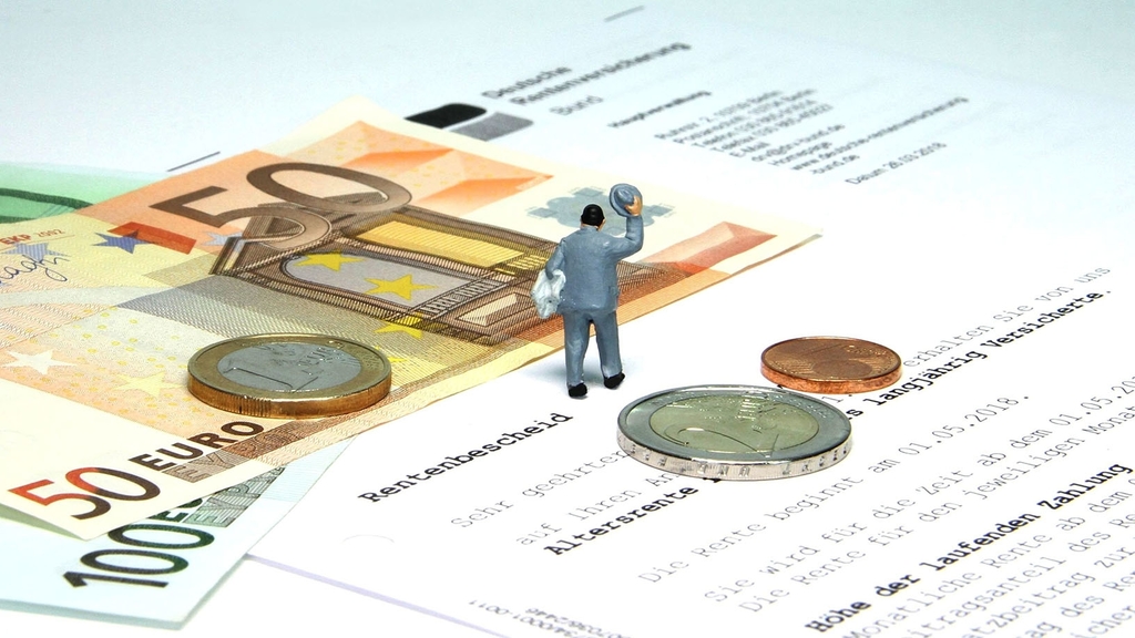 Vergrößerung des Bildes für Rentenbescheid, Geld und Miniaturnachbildung eines Menschen liegen auf einem Tisch.