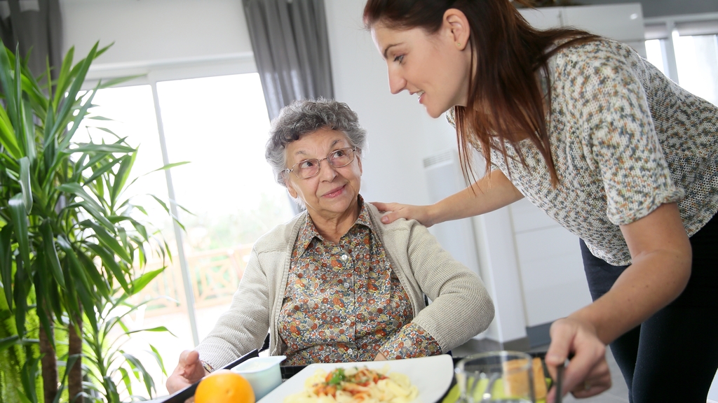 Vergrößerung des Bildes für Eine Seniorin bekommt Essen von einer Pflegerin serviert..