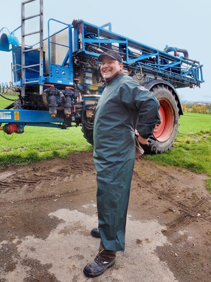 Vergrößerung des Bildes für Bild: Mann vor Landmaschine beim Anziehen einer Ärmelschürze.