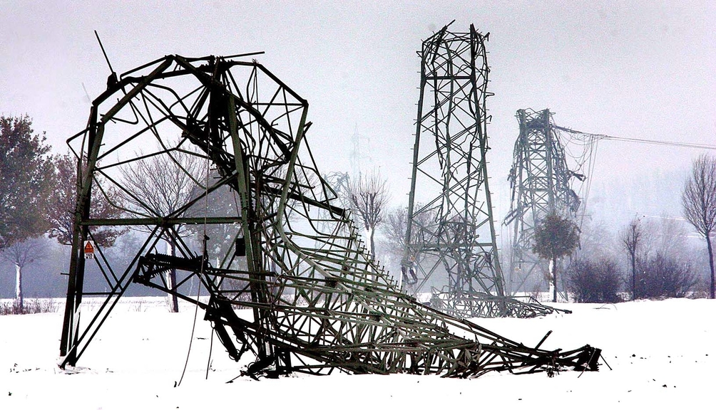 Vergrößerung des Bildes für in einer Schneelandschaft steht ein abgeknickter Strommast mit zerstörter Stromleitung..