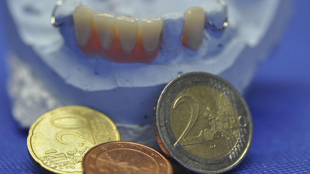 Vergrößerung des Bildes für Eine Zahnersatz Prothese. Davor liegen Geldmünzen.